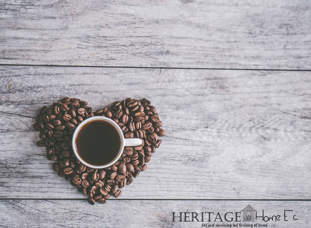cup of coffee in a heart-shaped pile of coffee beans on light wood background