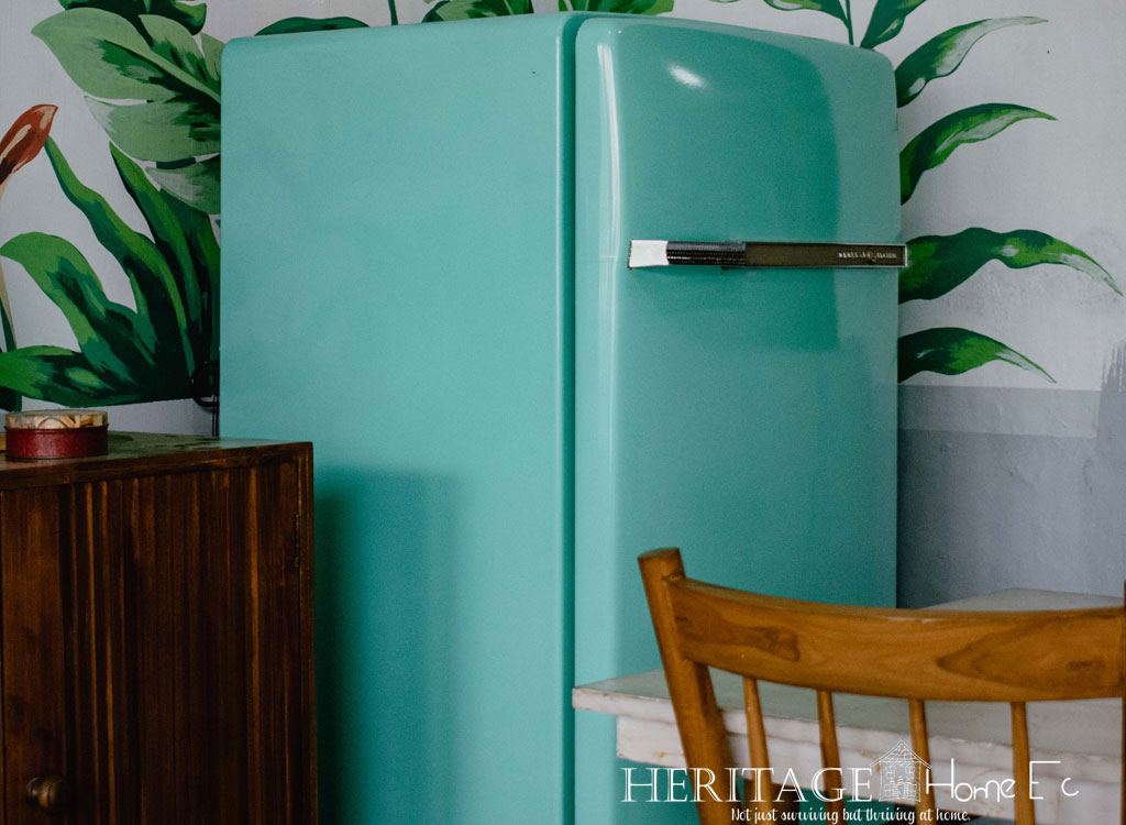 vintage teal refrigerator in kitchen with wooden chair and greenery mural