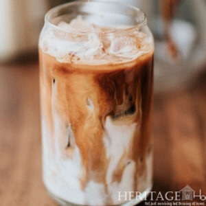 close up of iced coffee with swirled milk in glass on wood table