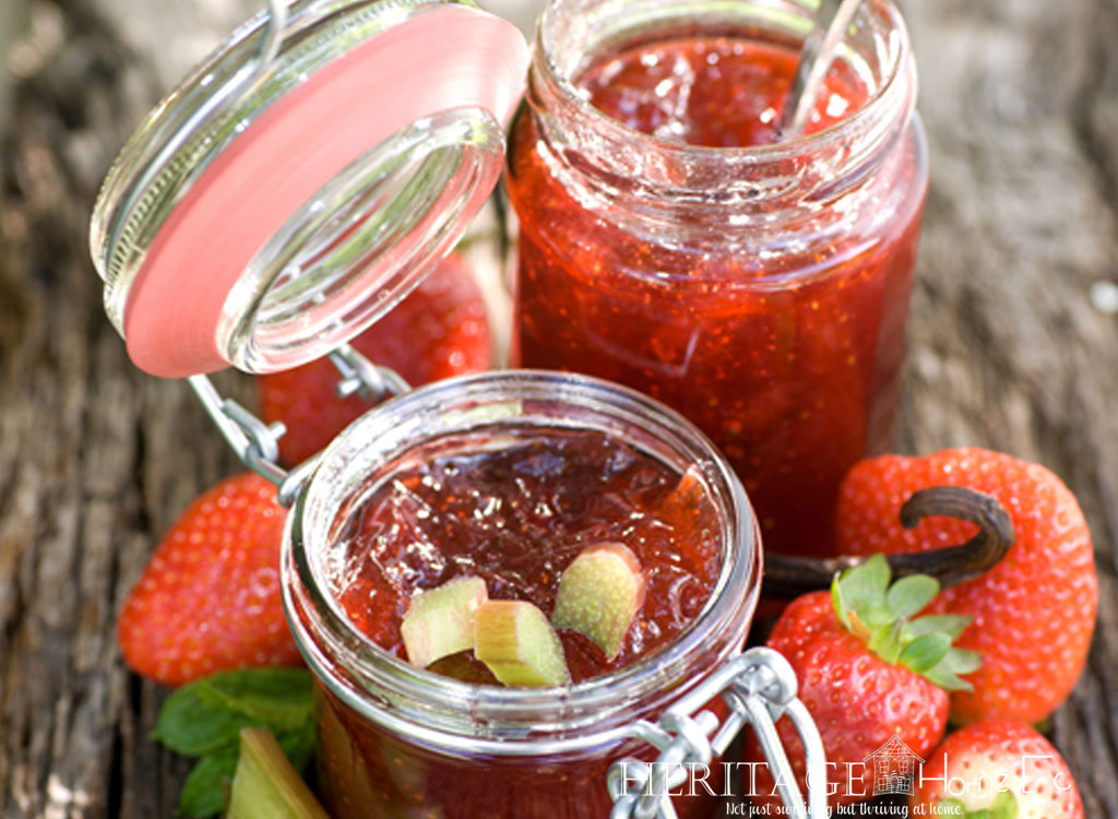strawberries and rhubarb surrounding jelly jars on a wooden background