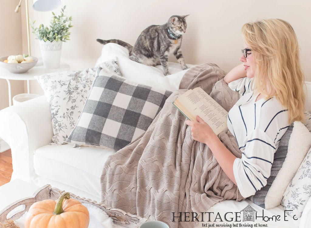 woman reading with throw blanket on couch with cat