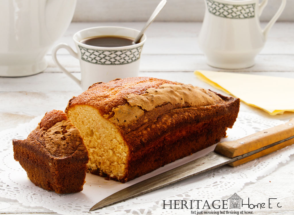 loaf of sponge cake on doily with knife and coffee cup