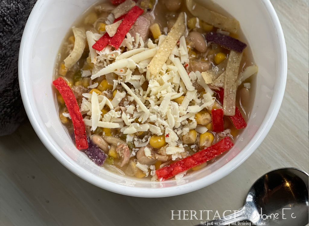 chicken chili in white bowl with soup spoon pepper jack cheese and tortilla strips