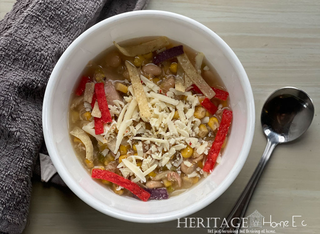 chicken chili in white bowl with soup spoon pepper jack cheese and tortilla strips