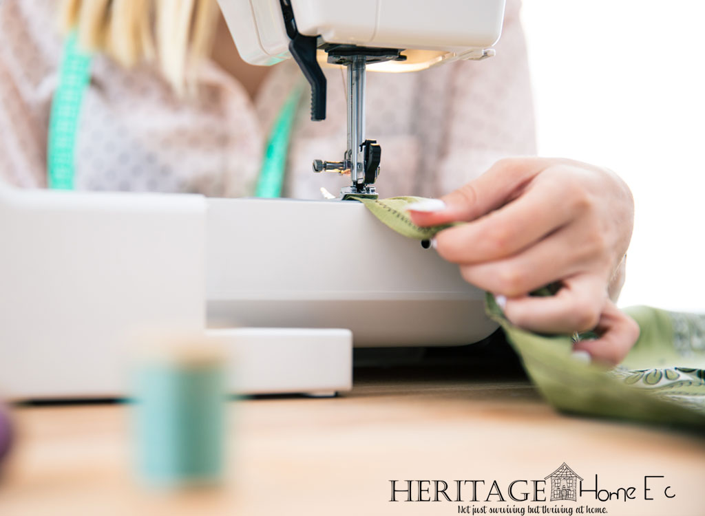 woman at sewing machine stitching green fabric with tape measure hanging from her neck