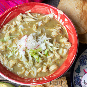 red bowl of Pozole Verde with radish garnish and avocado and tortilla chips