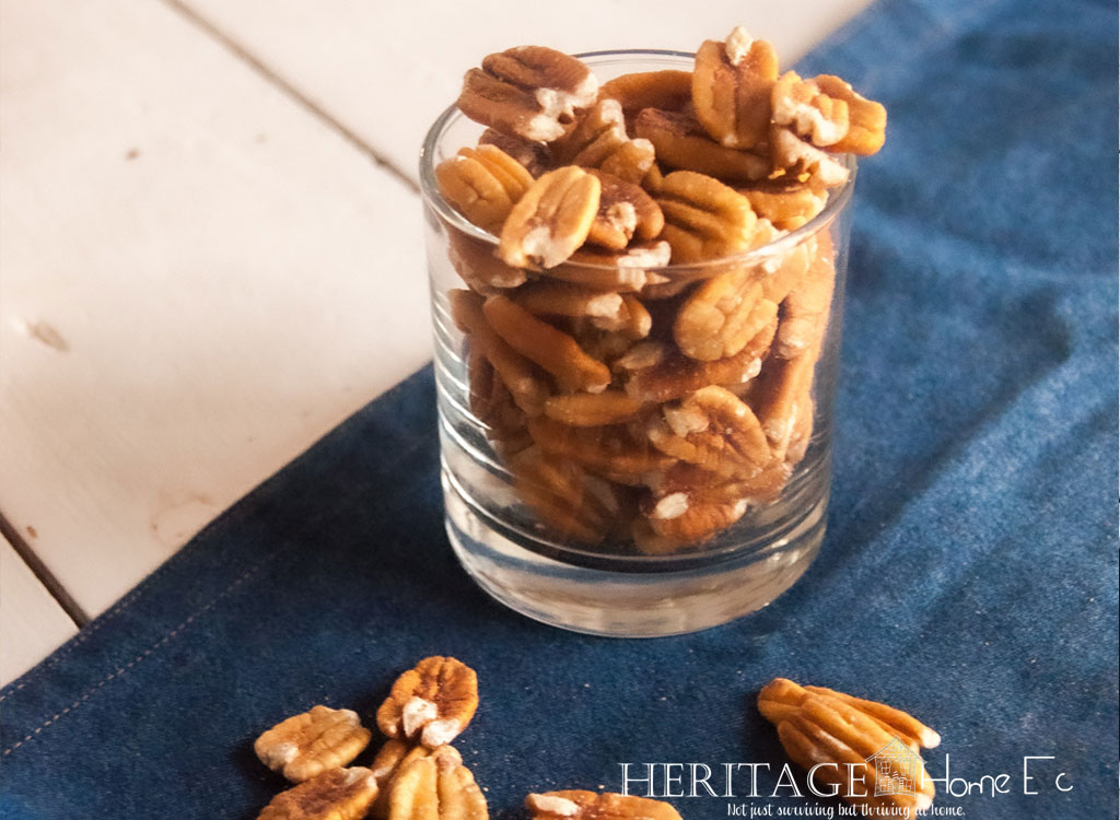 glass full of pecans with scattered nuts on blue cloth