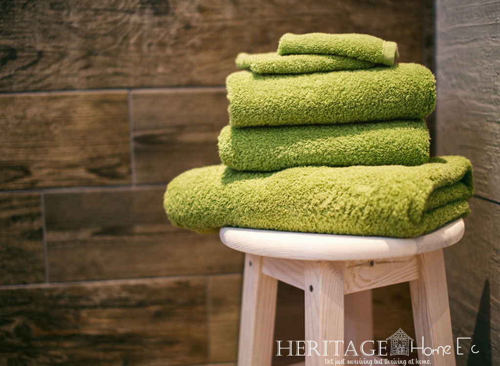 stack of green bath towels stacked on a stool with wood tile backdrop